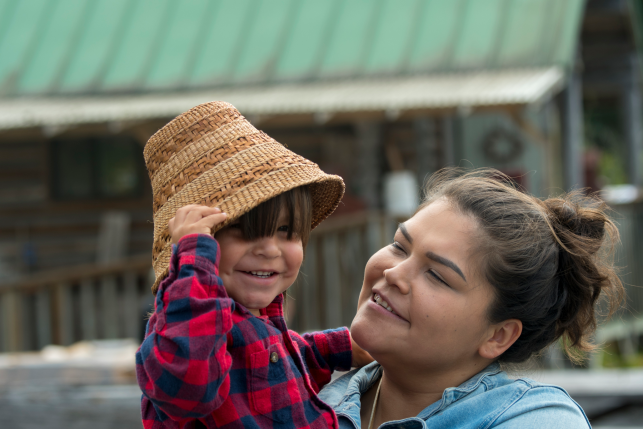 Portrait of a Tlingit mother with her small boy wearing a traditional woven hat.