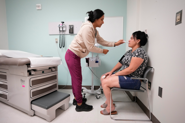 Medical assistant takes oral temperature of seated patient