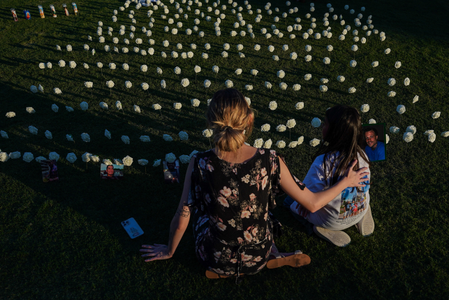 People sit on ground facing rows and rows of lit candles