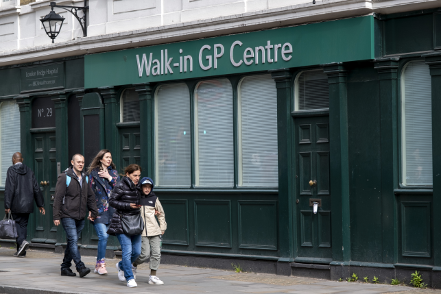 People walking in front of a green building with a sign that reads "Walk-in GP Centre"