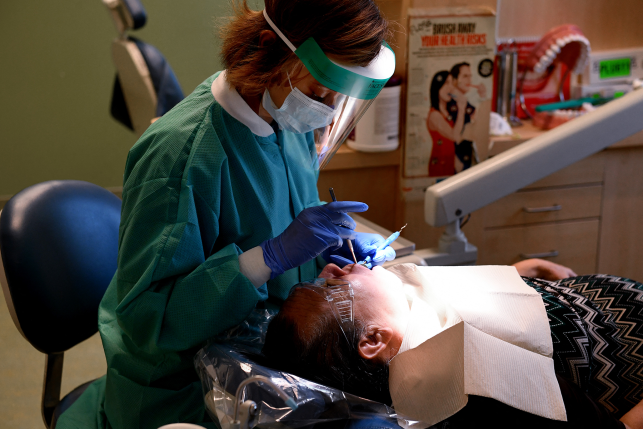 Dental hygienist in mask works on patient in chair