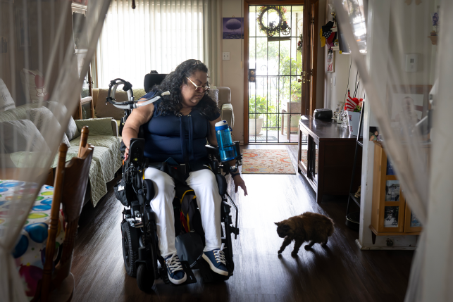 Woman in motorized medical wheelchair reaches to pet cat