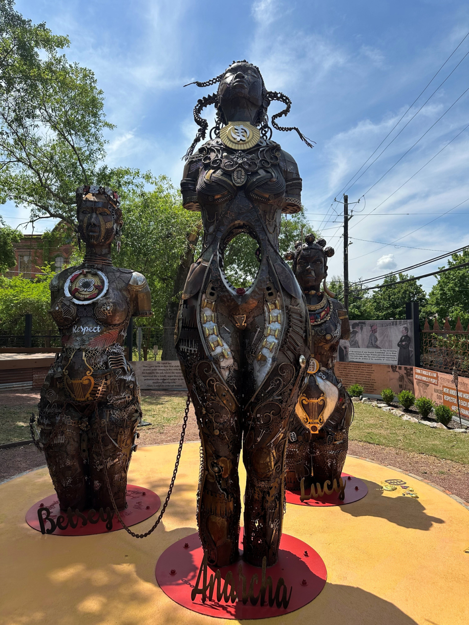 Three mixed media sculptural statues of women displayed in an outdoor area.