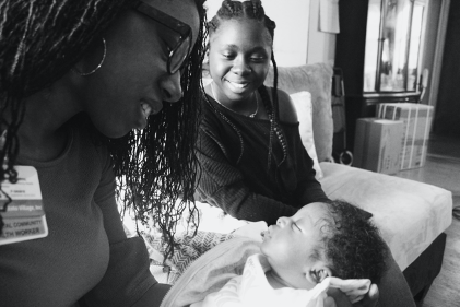 Perinatal community health worker sitting with mother and holding newborn baby
