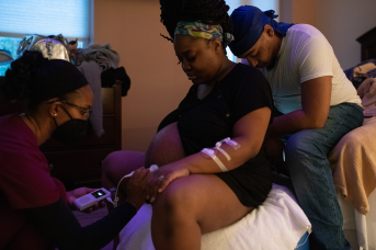 Nurses listens to fetal heartbeat of mother in labor, with father behind her
