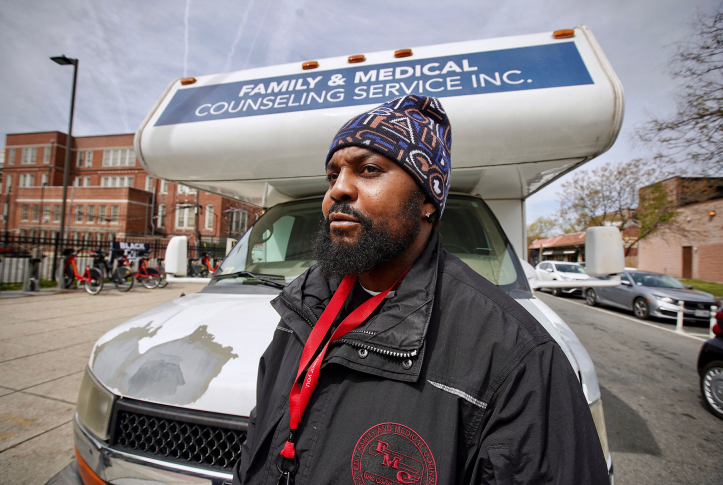Man in hat stands in front of Familly and Medical Counseling Service bus