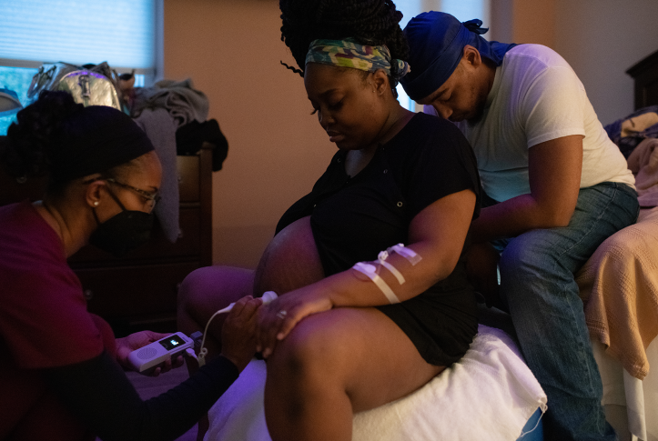 Nurses listens to fetal heartbeat of mother in labor, with father behind her