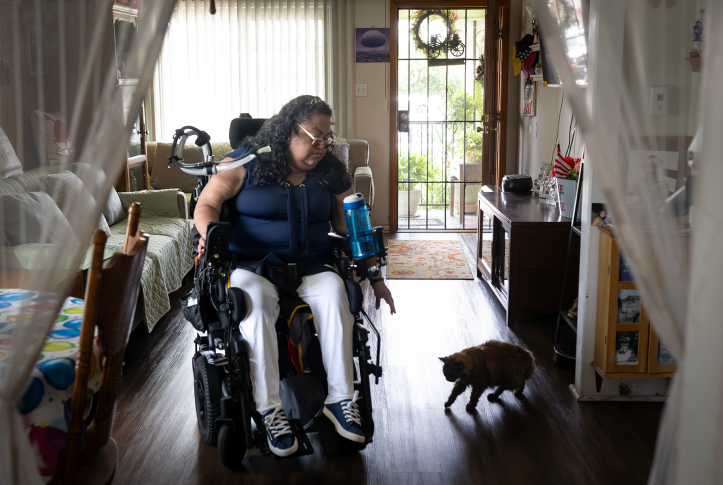 Woman in motorized medical wheelchair reaches to pet cat