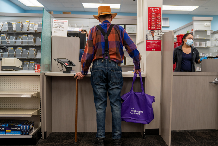 Elderly man with cane standing at pharmacy counter waiting for prescription
