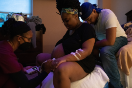 Nurses listens to fetal heartbeat of mother in labor, with father behind her