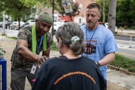 Two men handing supplies to a woman who is facing away from the camera.