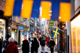 Swedish flag flies over busy street with pedestrians